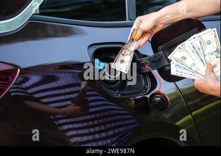 Hand der Frau, die Geld in den Tank des Autos steckt, Nahaufnahme, Konzept des teuren Kraftstoffs, Kraftstoffkrise Stockfoto