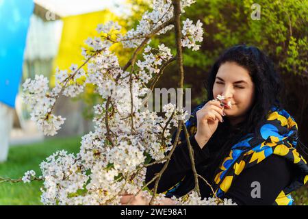Junge ukrainische Brünette, die im Frühjahr beim Spaziergang im Park das Aroma von Kirschblüten genießt Stockfoto