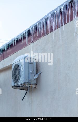 Der Conditioner ist mit Eiszapfen an einer gelben Wand bedeckt. Betrieb der Klimaanlage im Winter bei niedrigen Temperaturen. Kühlung, kalte Konzeptbild. Stockfoto