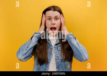 Porträt einer verängstigten jungen Frau, die mit erstaunlichem Gesichtsausdruck steht, mit großen Augen in die Kamera blickt, sehr überrascht ist und eine Jeansjacke trägt Stockfoto