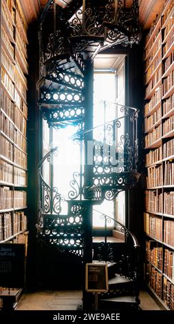 Verzierte, schmiedeeiserne Wendeltreppe in einer klassischen Bibliothek mit raumhohen Bücherregalen. Stockfoto