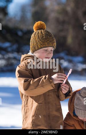 Lustiger kleiner Junge spaziert während eines Schneefalls. Winteraktivitäten im Freien für Kinder. Stockfoto