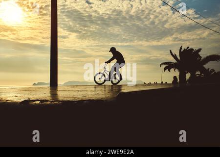 Die Silhouette ist nicht erkennbar von einem Kerl mit einem bmx-Fahrrad. BMX-Fahrer. Junger Mann, der bei Sonnenuntergang auf bmx-Fahrrad eine Rampensprungwelle macht Stockfoto