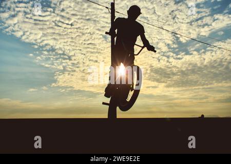 Silhouette nicht erkennbar junger Mann, der bei Sonnenuntergang auf bmx-Fahrrad Rampensprung macht. Stockfoto