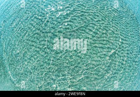 Wasser plätschert über den Sandstrand. Transparente blaue, klare Wasseroberfläche mit Spritzern. Wasserhintergrund, Wellen und Strömung mit Wellen. Blau Stockfoto