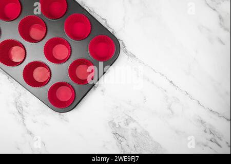 Ansicht von oben auf Cupcake-Pfanne und Silikonhüllen auf weißem Marmorhintergrund. Muffins und Cupcakes kochen, flach legen, Kopierraum. Stockfoto