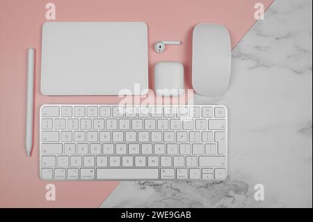 Draufsicht auf weiße Tastatur, Maus, Touchpad, Kopfhörertasche, Stift auf rosa und weißem Marmorhintergrund. Modernes Büro, Flachbett, Kopierraum. Stockfoto