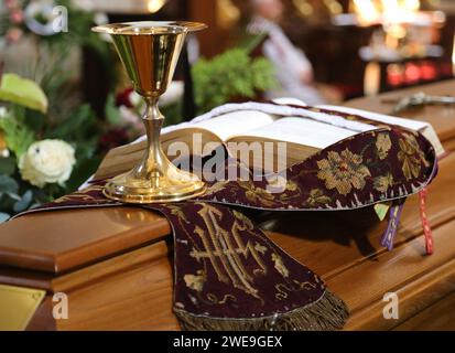Goldener Kelch und gepatchte, gestohlene und missliche Bücher, die während der katholischen Priesterbeerdigung auf den Sarg gelegt wurden. Stockfoto