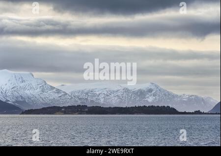 Das ruhige Bild fängt eine majestätische schneebedeckte Bergkette ein, die über dem ruhigen, reflektierenden Meereswasser unter einem bewölkten Abendhimmel aufragt. Stockfoto