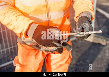 Nahaufnahme eines Bauherstellers, der einen Bohrer in einen Akku-Bohrhammer einbringt, um Löcher in der Straße an der vom Bauingenieur gekennzeichneten Stelle zu bohren Stockfoto