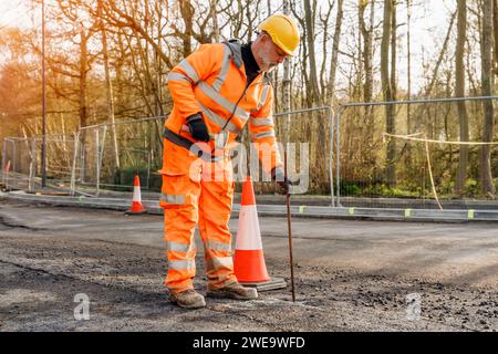 Bauarbeiter, der die Straße niederschlägt und bei Bauarbeiten Stahlstifte mit einem Klumpenhammer ausräumt. Der Baumeister hämmert während der Straßenfahrt Stahlstäbe in den Asphalt Stockfoto