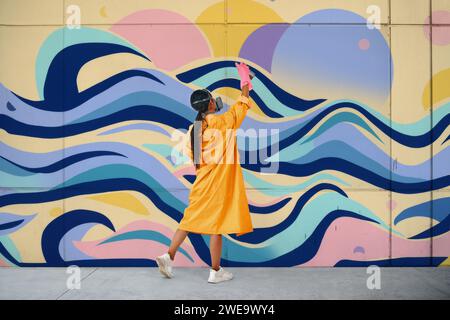 Weibliche Straßenmalerin in Atemmaske Malerei Bunte Graffiti an der Wand Moderne Kunst, städtisches Konzept. Stockfoto