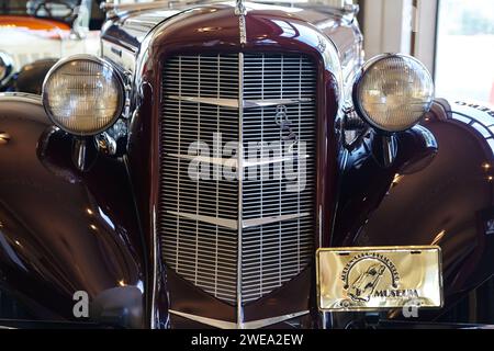 Glänzendes Maroon Oldtimer-Vorderteil mit verchromtem Kühlergrill und Scheinwerfern in Nahaufnahme Stockfoto