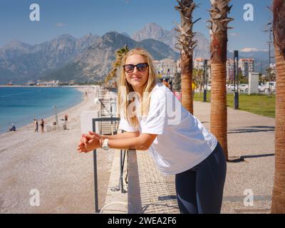 Junge attraktive Frau steht an der Seepromenade. Sportliches Lifestyle-Konzept, Spaziergang entlang des Ufers von Konyaalti in Antalya Stockfoto