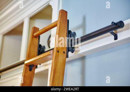 Moderne Holzleiter gegen weiße Wand mit Metallbeschlägen Stockfoto