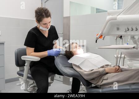 Ein Junge, der in einem Zahnarztstuhl sitzt, schaut eine Ärztin vor Angst an. Die erste ärztliche Vorsorgeuntersuchung eines Kindes bei einem Kinderzahnarzt. Stockfoto