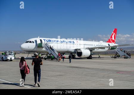 Passagiere, die auf dem Asphalt des Flughafens Nevsehir, Kappadokien, unter einem klaren blauen Himmel in Richtung eines Flugzeugs der Turkish Airlines laufen Stockfoto