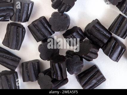 Schwarze Süßholzstücke, die auf weißer Oberfläche verstreut sind Stockfoto