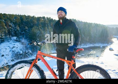 Fröhlicher, gutaussehender junger Mann, der Zeit zur freien Verfügung in der Natur verbringt, an der frischen Luft genießt und mit dem Fahrrad fährt Stockfoto