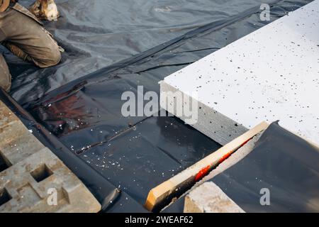 Baumeister legt Polystyrol-Dämmplatten auf Wasserabdichtungsmembran während des Bodenbaus. Energiesparkonzept Stockfoto