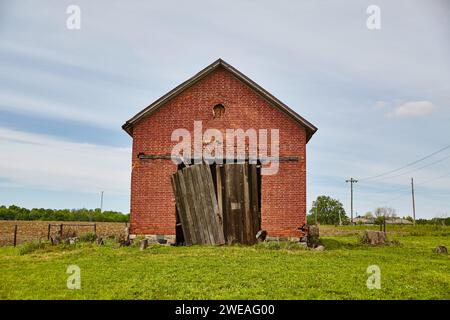 Verwitterte rote Ziegelscheune in ländlicher Landschaft mit blauem Himmel Stockfoto