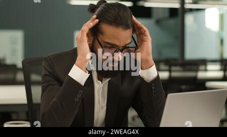 Arabian Mann indischer Büroangestellter am Arbeitsplatz Tisch ethnischer Unternehmer Mann männlicher Geschäftsmann müde Kopf halten Laptop Problem Stockfoto