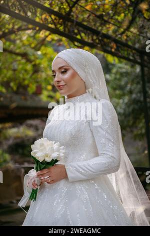 Junge Braut in weißem Spitzenkleid im Freien mit weißem Tulpenstrauß Stockfoto