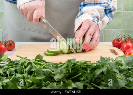 Gemüse mit Kräutern und weiblichen Händen schneiden eine Gurke in einen Salat. Kopierbereich. Stockfoto