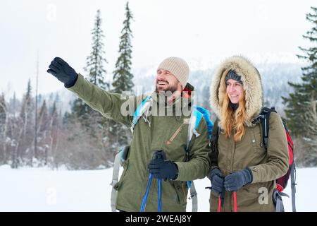 Glückliches, optimistisches Paar mittleren Alters, das zusammen in den Bergen reist, aufgeregter männlicher Entdecker, der auf die Landschaft zeigt Stockfoto
