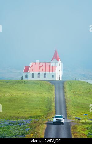 Wunderschöne heilige Ingjaldsholskirkja Kirche und Auto fahren auf der Straße im Nebel im Sommer auf der Snaefellsnes Halbinsel, Island Stockfoto