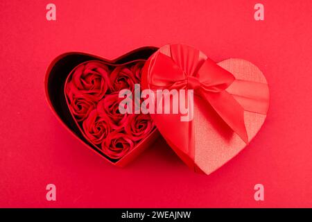 Herzförmige Geschenkbox mit Rosen zum Valentinstag auf rotem Hintergrund Stockfoto