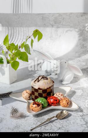 Osterdekor. Osterstillleben mit bunten Osterkuchen, Eiern auf Kaninchen-Dessertteller. Traditionelles Ostergeschenk auf festlichem Tisch, dekoriert mit spr Stockfoto