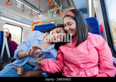 Zwei junge Freundinnen, eine mit dem Kopf auf der Schulter, die in öffentlichen Verkehrsmitteln unterwegs ist und telefoniert Stockfoto