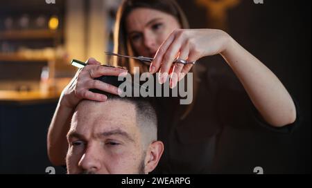 Junge Friseur weibliche Hände mit Schere und Kamm Friseur Close-up-Bild in modernem Barbierladen in schwachem, schwarzem Stil. Haarpflegedienst Stockfoto
