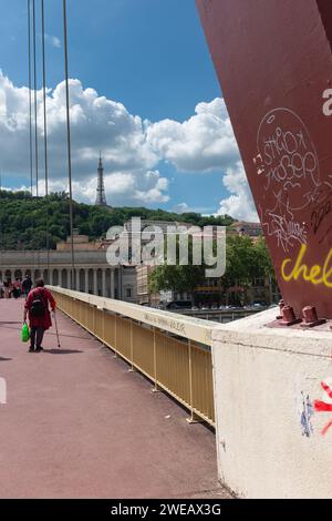 Lyon, Frankreich, 2023. Eine Dame überquert die Fußgängerbrücke Palais de Justice mit der Tour Métallique de Fourvière im Hintergrund (vertikal) Stockfoto