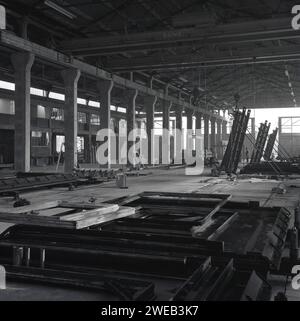 1960er Jahre, historisches Inneres eines großen „Hangar“-Gebäudes mit Grantry, in dem Fertigbetonplatten hergestellt werden, England, Großbritannien. Name oben auf der Gantry, Rowlan Priest, Cradley Heath, SWL 10 Tonnen. In Großbritannien in den späten 50er und 60er Jahren wurden große Turm- und Büroblöcke aus vorgegossenen Betonplatten errichtet, was eine schnellere und kostengünstigere Konstruktion und eine hervorragende Feuerbeständigkeit bedeutet. Stockfoto