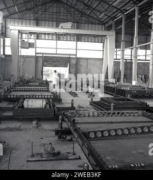 1960er Jahre, historisches Inneres eines großen „Hangar“-Gebäudes mit Grantry, in dem Fertigbetonplatten hergestellt werden, England, Großbritannien. Name oben auf der Gantry, Rowlan Priest, Cradley Heath, SWL 10 Tonnen. In Großbritannien in den späten 50er und 60er Jahren wurden große Turm- und Büroblöcke aus vorgegossenen Betonplatten errichtet, was eine schnellere und kostengünstigere Konstruktion und eine hervorragende Feuerbeständigkeit bedeutet. Stockfoto