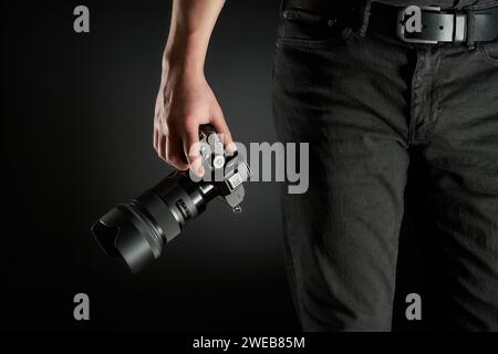 Ein junger Fotograf hält eine spiegellose Kamera in seinem Handstudio Stockfoto