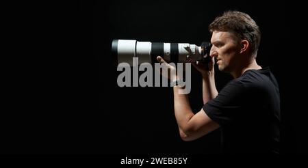 Junges Foto mit Kamera und großem weißem Objektiv isoliert auf schwarzem Hintergrund Stockfoto