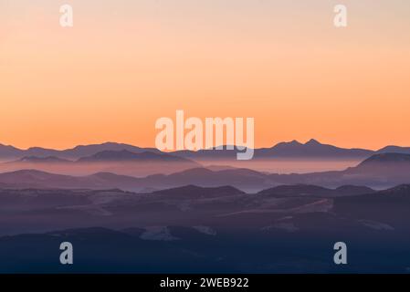 Hochgebirge in dichtem Nebel. Schichten von Bergen im Dunst bei Sonnenuntergang. Mehrlagige nebelige Berge. Stockfoto