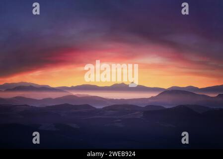 Berge im Nebel bei Sonnenuntergang. Dramatische Landschaft mit bewölktem Himmel, Tal, Nebel, Bergen und hellem Sonnenschein unter Berggipfeln. Stockfoto