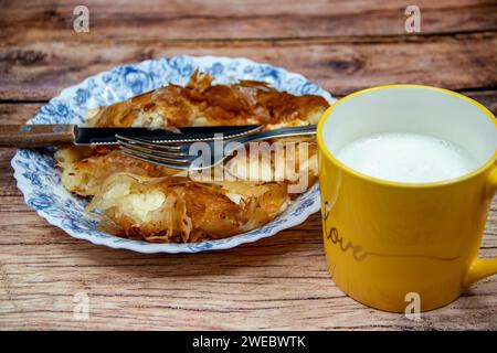 Serbisches Gericht namens Burek (Käsekuchen), serviert zum Frühstück auf dem Teller mit Besteck und frischem hausgemachtem Joghurt in der Tasse Stockfoto