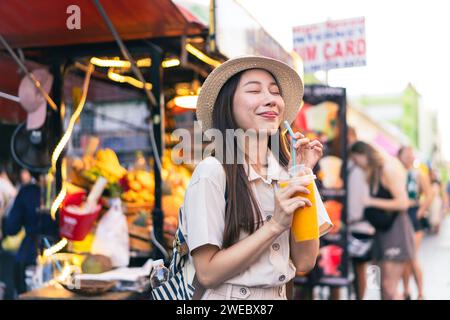 Junge asiatische Reisetäuferin kaufte einen frisch zubereiteten Saft und spazierte auf dem Markt im Freien in Bangkok in Thailand. Reisende, Sommerferien und Tourismus Stockfoto