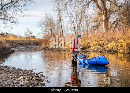 Der ältere männliche Paddler startet sein aufblasbares Packraft im Frühjahr auf einem Fluss - dem Poudre River im Norden von Colorado Stockfoto