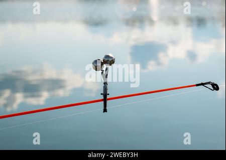 Signalglocke an der Spitze der Angelrute. Beißalarm vor dem Hintergrund der Reflexion von Wolken im Wasser. Stockfoto