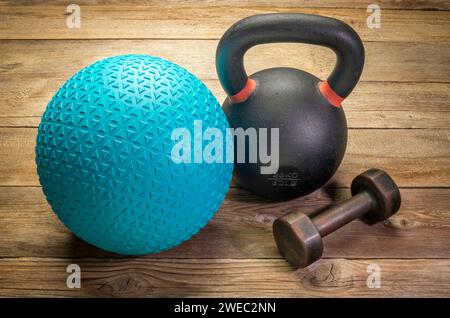 Schwerer, mit Sand gefüllter Gummiball, eine Eisenhantel und eine kleine Hantel auf rustikalem Holzhintergrund, Training, Training und Fitnesskonzept Stockfoto