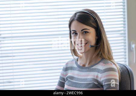 Ein Kundendienstmitarbeiter mit einem Headset lächelt herzlich und sorgt für eine freundliche Präsenz in einer professionellen Umgebung Stockfoto