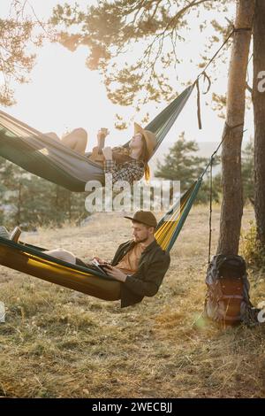 Ein Mann und ein Mädchen entspannen sich in Hängematten in einem Kiefernwald bei Sonnenuntergang. Stockfoto