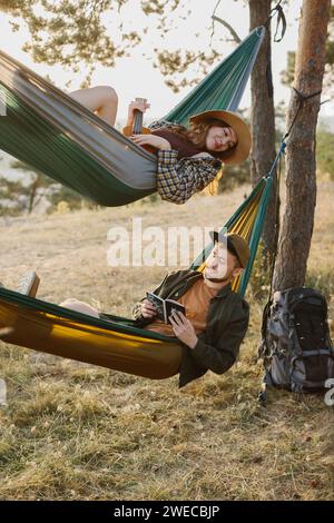 Ein Mann und ein Mädchen entspannen sich in Hängematten in einem Kiefernwald bei Sonnenuntergang. Stockfoto