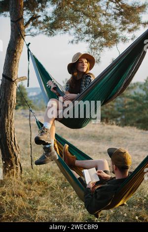 Ästhetische Ruhe. Ein wunderschönes Mädchen und ihr Freund entspannen sich bei Sonnenuntergang in Hängematten. Stockfoto